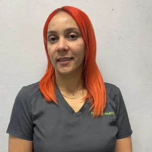 mirka is smiling wearing a merry maids uniform standing in front of a grey wall